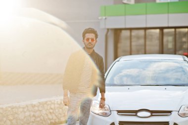 Güney Asyalı ya da Hintli erkek, araba yıkamada beyaz aracının yanında kırmızı gözlük takıyor..