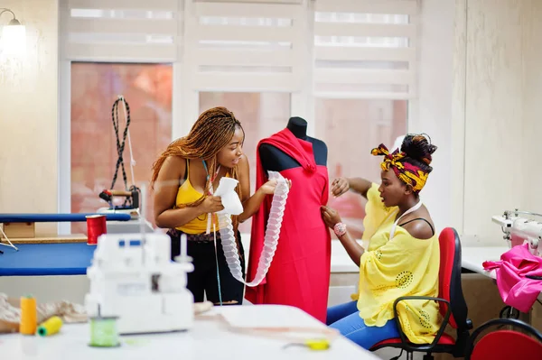Two african dressmaker woman designed new red dress on mannequin at tailor office. Black seamstress girls.