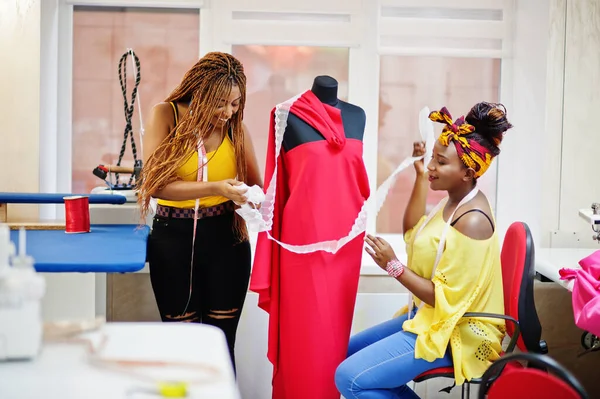 Two african dressmaker woman designed new red dress on mannequin at tailor office. Black seamstress girls.