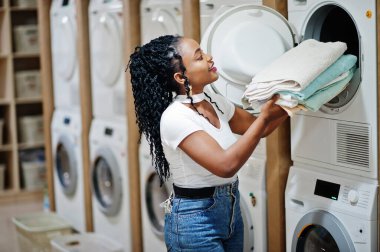 Çamaşır makinesinin yanında havluları olan neşeli Afro-Amerikalı kadın..