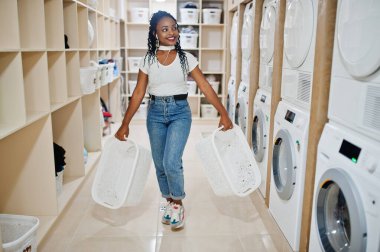 Çamaşır makinesinin yanındaki neşeli Afro-Amerikalı kadın self-servis çamaşırhanesinde cep telefonundan müzik dinliyor..