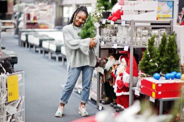 Afrikalı bir kadın modern bir ev mobilyası mağazasında yeni yıl eşyalarını seçiyor. Noel temalı alışveriş.