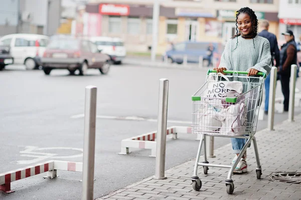 African woman with shopping cart trolley posed outdoor market near car parking.