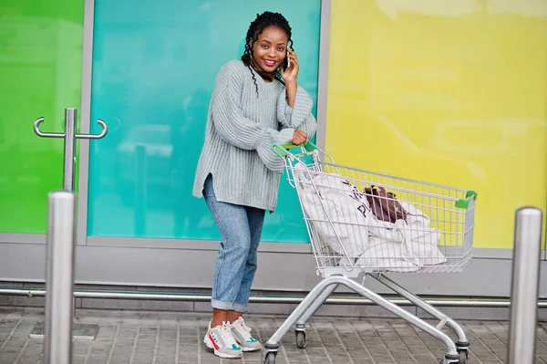 African woman with shopping cart trolley posed outdoor market and speak on phone.