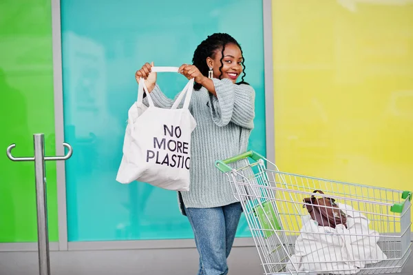 No more plastic. African woman with shopping cart trolley show eco bag posed outdoor market.