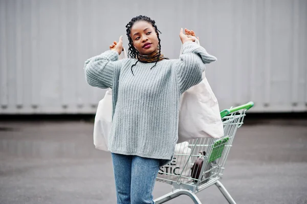 No more plastic. African woman with shopping cart trolley and eco bags posed outdoor market.