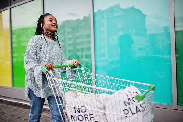 No more plastic. African woman with shopping cart trolley posed outdoor market.