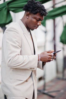 Bej rengi eski okul takımlı, cep telefonu olan şık bir afro adam. Üstü başı çıplak, şık, genç Afrikalı bir erkek..