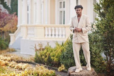 Bej rengi eski okul takım elbiseli şık bir afro adam. Üstü başı çıplak, şık, genç Afrikalı bir erkek..