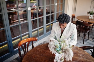 Eski bej takım elbiseli şık afro adam cep telefonuyla kafede oturuyor. Üstü başı çıplak, şık, genç Afrikalı bir erkek..