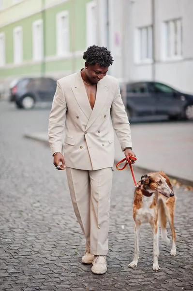 Stylish afro man in beige old school suit with Russian Borzoi dog. Fashionable young African male in casual jacket on bare torso.