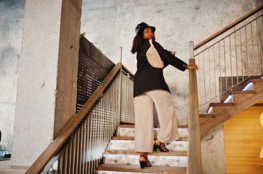 Çekici Afrikalı Amerikalı kadın manken siyah ceketli, şapkalı ve bel çantalı boş zamanlarında kafede dinleniyor..