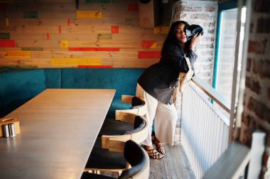 Çekici Afrikalı Amerikalı kadın manken siyah ceketli ve boş zamanlarında kafede dinleniyor..