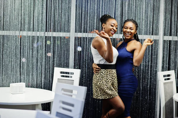 Two african woman in dress posing at restaurant.
