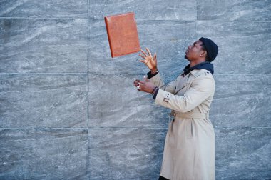 Siyah şapkalı ve bej ceketli, elinde klasörle dışarıda poz veren yakışıklı Afrikalı Amerikalı adam..