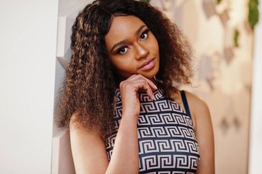 Çekici, zarif, uzun kıvırcık saçlı Afro-Amerikan kadının kapalı kafede poz verdiği portreyi yakından çek..