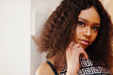 Çekici, zarif, uzun kıvırcık saçlı Afro-Amerikan kadının kapalı kafede poz verdiği portreyi yakından çek..