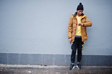 Afrikalı bir adam soğuk havada gri duvara karşı poz verirken ceketini giyer ve saatlerine bakar..