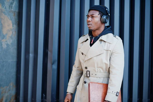 ヘッドフォンを持つアフリカ系アメリカ人男性 帽子を着用し 鋼の背景に音楽を聞いてコート — ストック写真