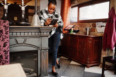 Kareli pelerinli Afrikalı kadın elinde menüyle nargile kafede poz verdi..