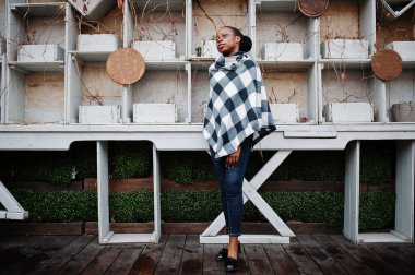 Kareli pelerinli ve gözlüklü Afrikalı kadın dışarıda poz verdi..