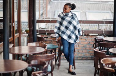 Kareli pelerinli Afrikalı kadın açık kafe terasında poz verdi..