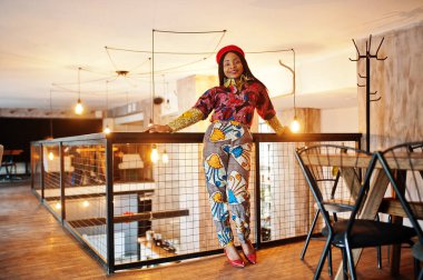 Coşkulu Afrikalı Amerikalı kadın moda renkli kıyafetler içinde, rahat bir kafede kırmızı bereli..