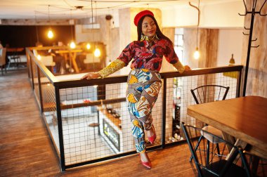 Coşkulu Afrikalı Amerikalı kadın moda renkli kıyafetler içinde, rahat bir kafede kırmızı bereli..