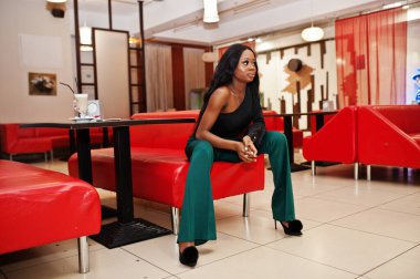 İnce, Afro-Amerikan modeli siyah bluz ve Çin kafesinde poz verilen yeşil uzun bacaklı pantolon giyiyor..