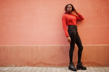 Kırmızı balıkçı yaka giyen kıvırcık saçlı bir kadının portresi gül duvarına poz veriyor..