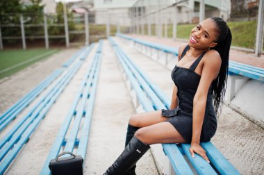 Stadyumdaki tribünde siyah giyinmiş şık, seksi, Afro-Amerikalı bir kadın..