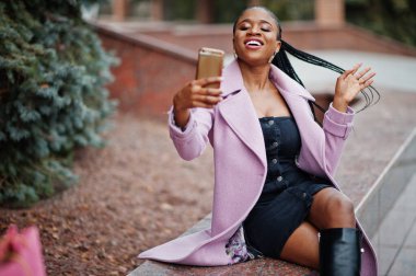 Genç, şık, afro-amerikan bir kadın. Moda kıyafeti giyiyor, cep telefonu var..