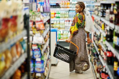 Geleneksel giysiler ve duvak giyen mutlu Afrikalı kadın markette ürün arıyor, süpermarketten alışveriş yapıyor. Marketten yiyecek alan Afro siyahi kadın kostümcü..