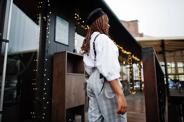 African american woman in overalls and beret walking out the door in outdoor terrace with christmas decorations.