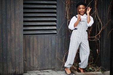 Tulumlu ve bereli Afro-Amerikalı kadın tahta arka planda poz vermiş..