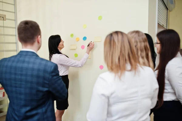 Young business people group of bank workers have meeting and working in modern office, pointing on wall with glued colorful paper notes.