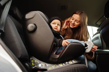 Arabada genç bir anne ve çocuk var. Sandalyeye bebek koltuğu. Güvenli sürüş kavramı.