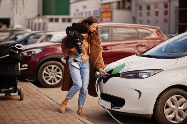 Elektrikli benzin istasyonunda çocuklu genç bir anne elektro arabayı şarj ediyor..