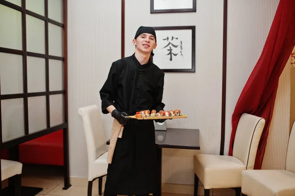 プロの料理人が寿司や日本の伝統料理のレストランでロールと黒で身に着けています — ストック写真