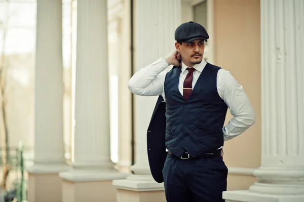 Portrait of retro 1920s english arabian business man wearing dark suit, tie and flat cap.