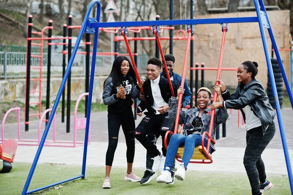 Young millennials african friends on playground, slide and swing. Happy black people having fun together. Generation Z friendship concept.