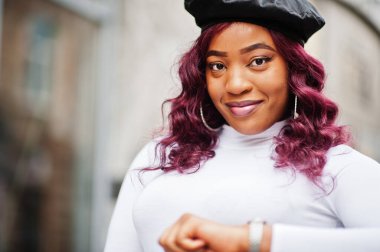 Büyük anne artı Afrikalı Amerikan modeli siyah bereli ve deri etekli. Dışarıda poz vermiş. El saatlerine bakıyor..