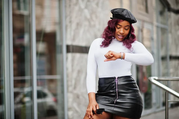 Big mama plus size african american model in black beret and leather skirt posed outdoor looking time at hand watches.