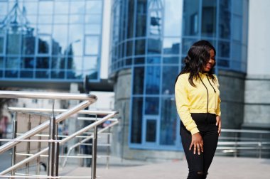 Sarı kapüşonlu Amerikalı hippi kız mavi pencereli ofis binasına karşı poz veriyor..