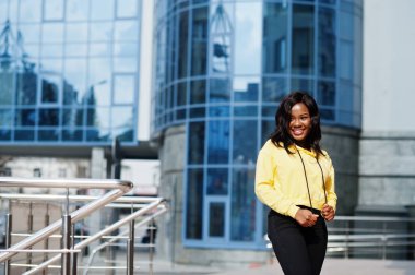 Sarı kapüşonlu Amerikalı hippi kız mavi pencereli ofis binasına karşı poz veriyor..