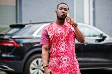 Siyahi bir gencin portresi, Afrikalı geleneksel kırmızı renkli giysiler ve cep telefonu..