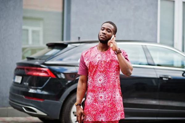 Siyahi bir gencin portresi, Afrikalı geleneksel kırmızı renkli giysiler ve cep telefonu..