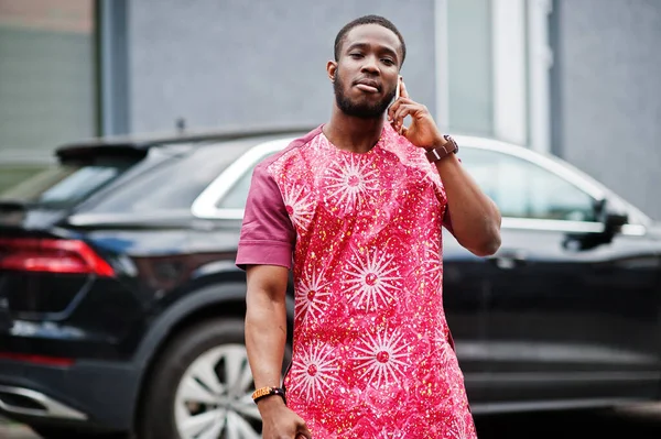 Siyahi bir gencin portresi, Afrikalı geleneksel kırmızı renkli giysiler ve cep telefonu..