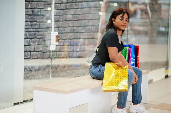 African-american woman sitting with coloured shopping bags in mall shopping center.