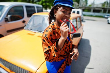 Güneş gözlüklü güzel Afrikalı Amerikalı kadın turuncu klasik eski arabanın yanında duruyor..